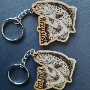 Drewniany brelok przestawiający wygrawerowanym wizerunek pstrąga wyskakującego z wody, z imieniem Krzysiek